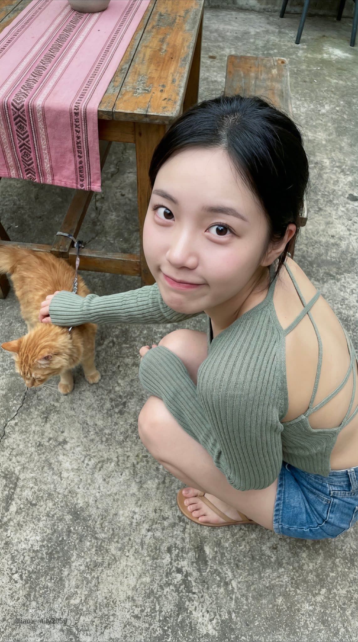 A young Asian woman sits crouched in a concrete courtyard.
